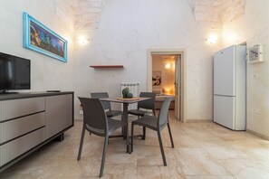 Eine kleine Küche mit Esstisch, Stühlen, Fernseher und Kühlschrank.