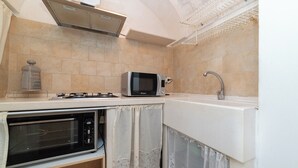 Een compacte keuken met een ingebouwde oven, een magnetron, een gasfornuis en een spoelbak.