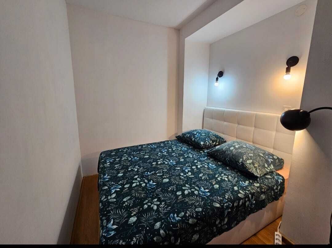 Un dormitori petit i ben ordenat, amb un llit, una tauleta de nit i una làmpada penjada a la paret.