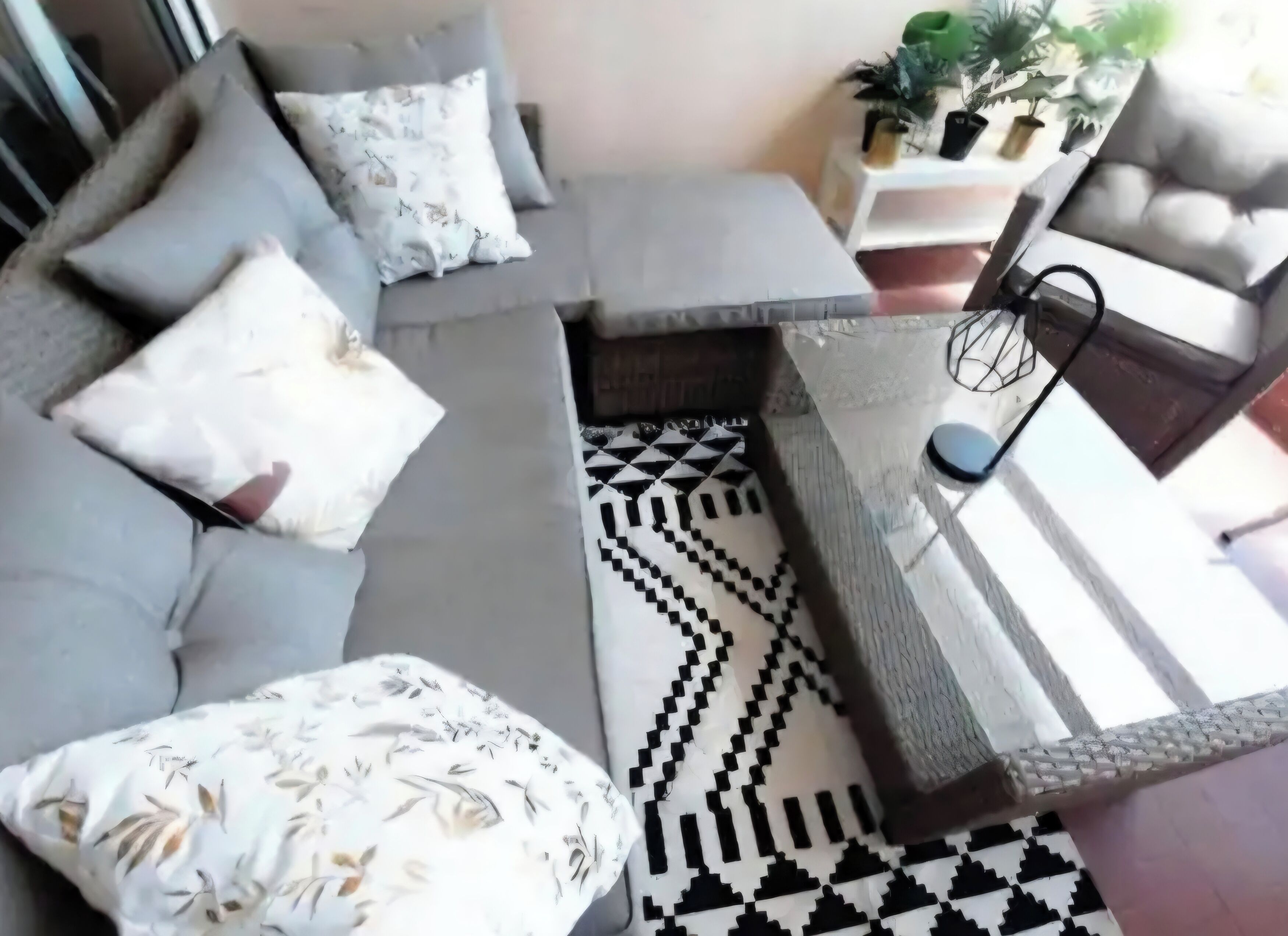 A modern living room with a grey sofa, patterned cushions, a black and white geometric rug, and a side table with a lamp.