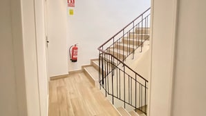 Un pasillo que conduce a una escalera, con un extintor en la pared.