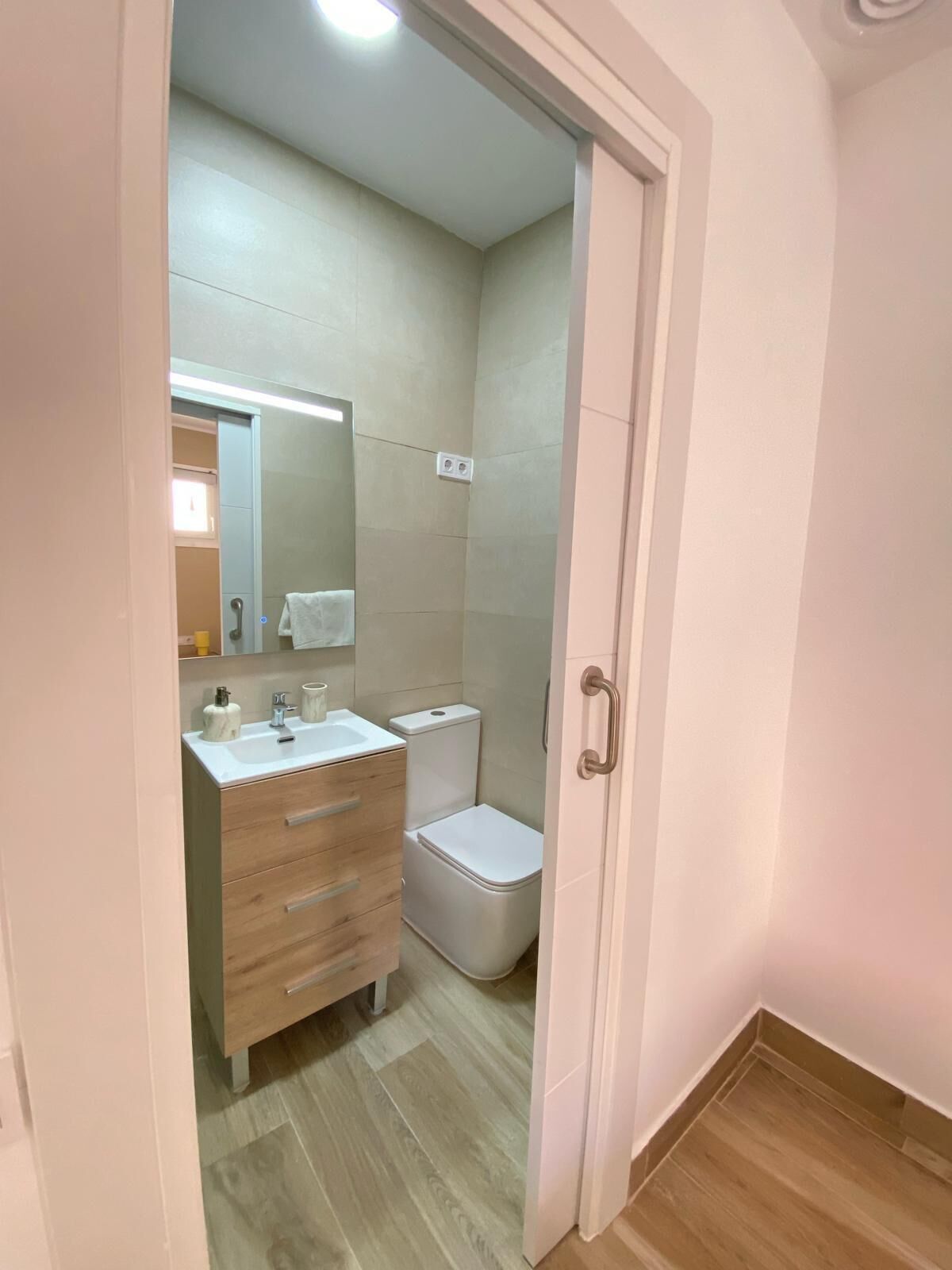 Un baño con tocador de madera, inodoro y espejo.
