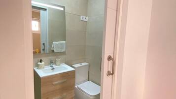 Un baño con tocador de madera, inodoro y espejo.