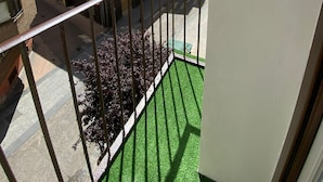 Un balcón con vistas a edificios cercanos, cielo despejado y una zona de césped artificial verde.