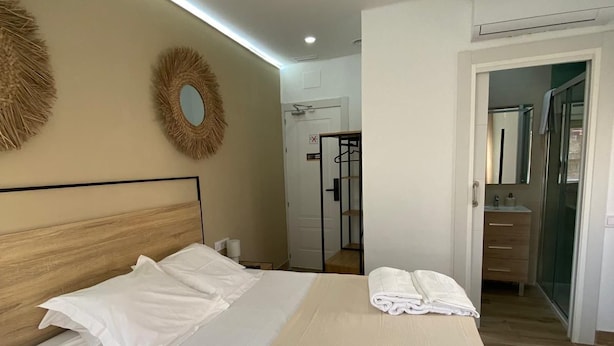 Una cama bien hecha con cabecera de madera, ventilador de techo y espejo fijado a la pared.