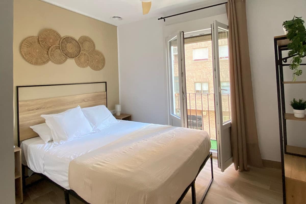 A bedroom with a bed, ceiling fan, and a view of the outside.