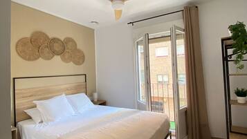 A bedroom with a bed, ceiling fan, and a view of the outside.