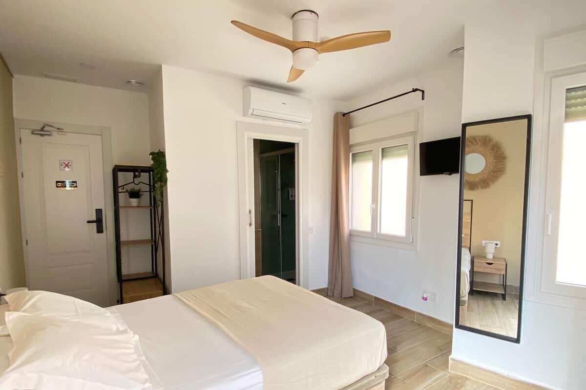 A bedroom with a bed, a ceiling fan, a TV, and a mirror.