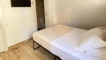 Un dormitorio con una cama, ventilador de techo, equipo de aire acondicionado, televisor y una mesita de noche con control remoto y una taza.