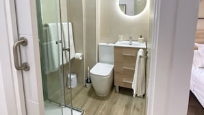 Un baño moderno con cabina de ducha de vidrio, un inodoro, un lavabo con espejo y piso de madera.