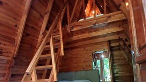 Una cabaña de madera con habitación en lo alto, una escalera de madera, una cama, un aparador y una alfombra estampada.