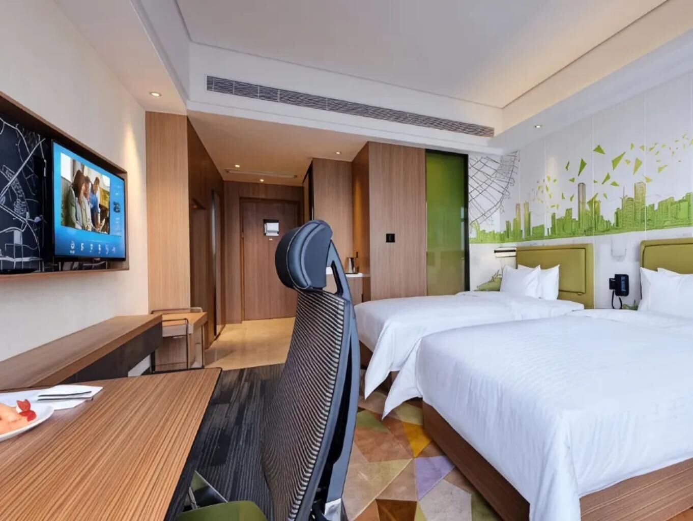 Een hotelkamer met twee bedden, een bureau, een stoel, een televisie en een stadsgezicht muurschildering.