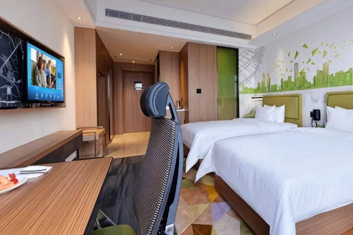 Une chambre d’hôtel avec deux lits, un bureau, une chaise, une télévision et une fresque murale représentant un paysage urbain.