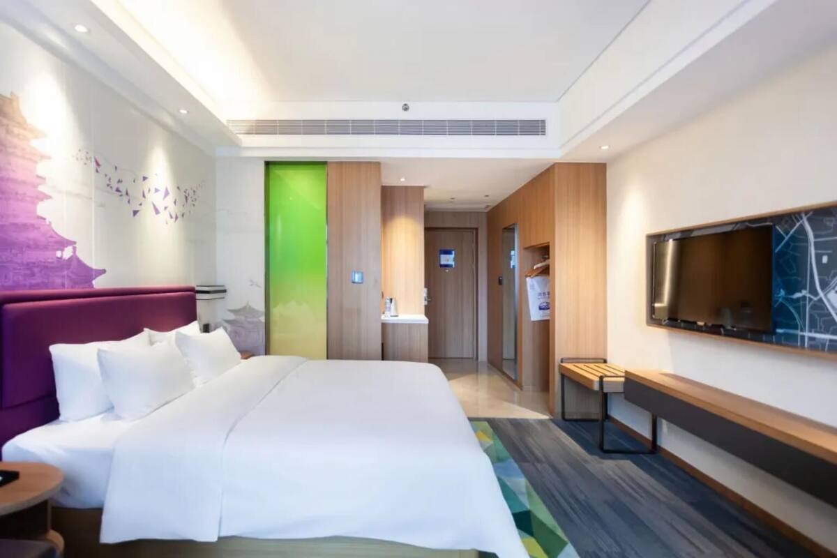 Une chambre d’hôtel moderne, dotée d’un grand lit, d’un bureau, d’une télévision et d’une salle de bain visible à travers une porte.