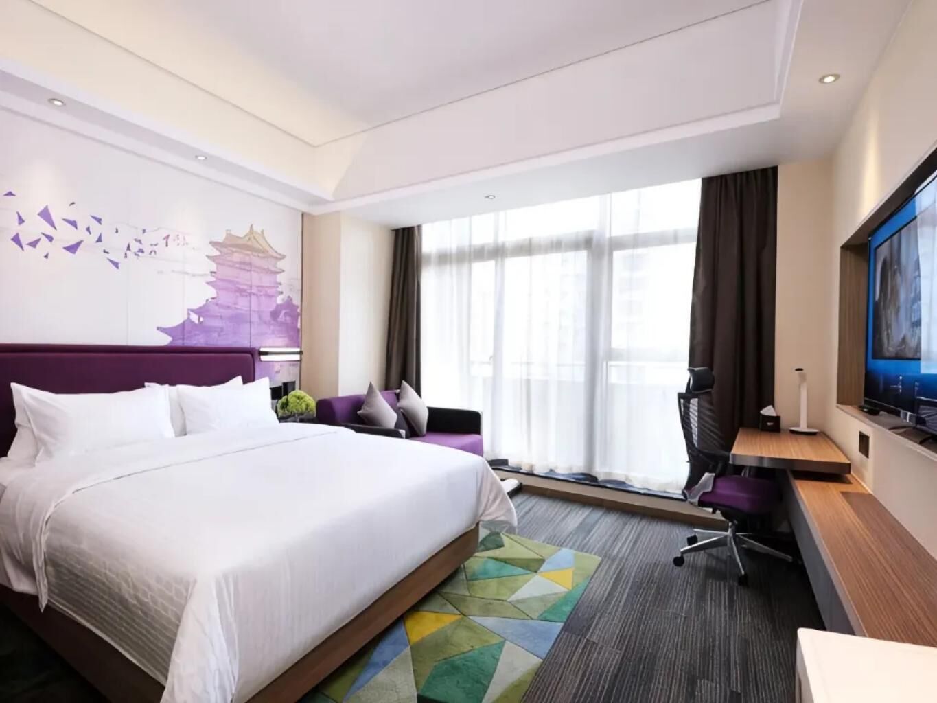 Een hotelkamer met een groot bed, een bureau, een stoel, een televisie en een raam met gordijnen.