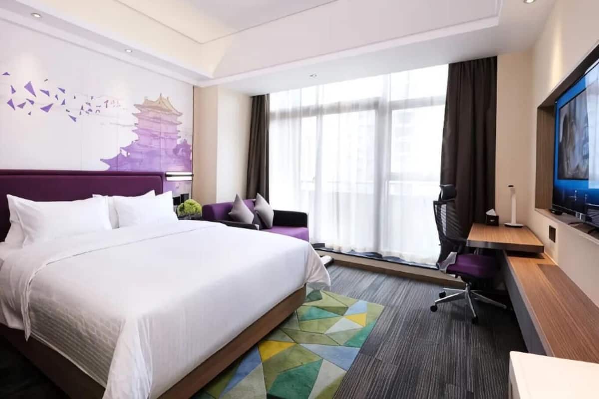 Une chambre d’hôtel avec un grand lit, un bureau, une chaise, une télévision et une fenêtre avec des rideaux.