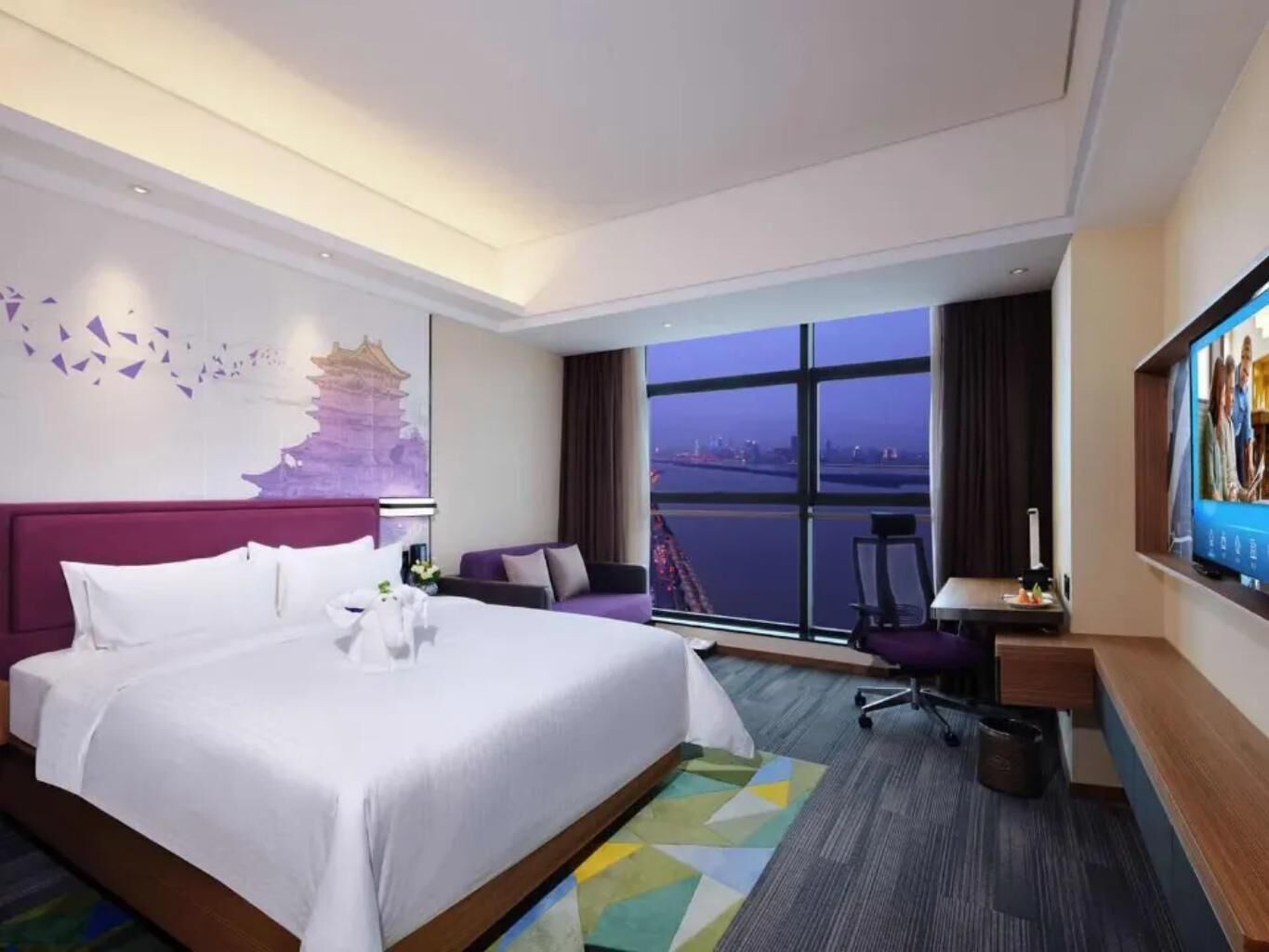 Hotelkamer met een groot bed, een bureau, een stoel, een televisie en een raam met uitzicht op de stad.