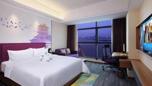 A hotel room with a large bed, a desk, a chair, a TV, and a window with a city view. - Hampton by Hilton China (Nanchang)