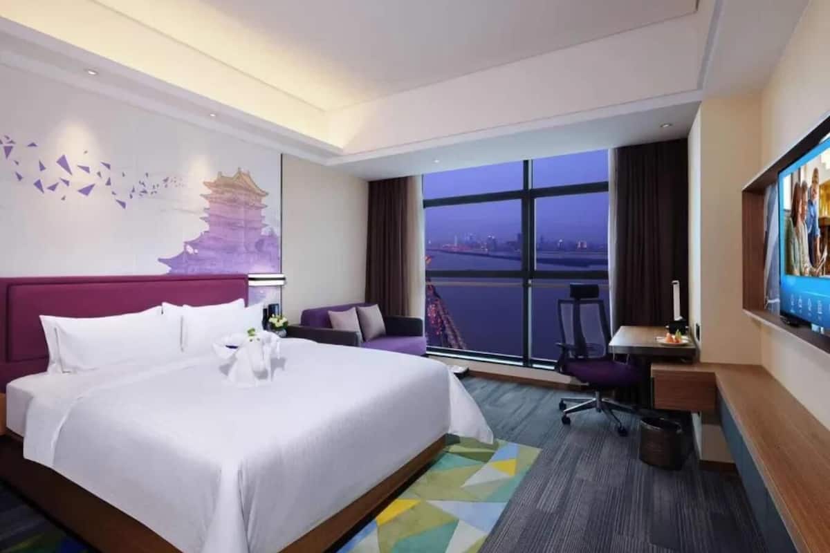 Une chambre d’hôtel avec un grand lit, un bureau, une chaise, une télévision et une fenêtre donnant sur la ville.