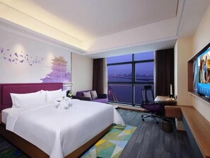 Hotelkamer met een groot bed, een bureau, een stoel, een televisie en een raam met uitzicht op de stad.