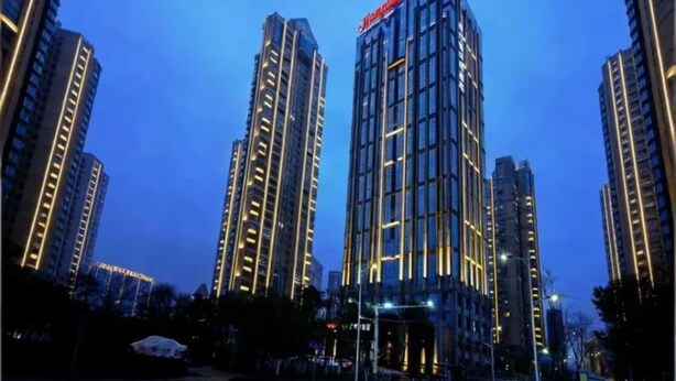 A high-rise building with a prominent sign at the top, surrounded by other tall structures. - Hampton by Hilton China (Nanchang)