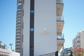 Un bâtiment moderne, orné d’une enseigne bien visible indiquant « PEARL PREMIUM SUITES », avec une architecture verticale, des balcons et un ciel dégagé en arrière-plan.