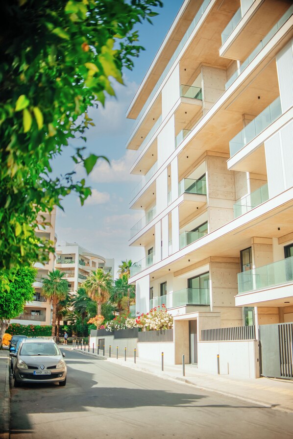Un immeuble à plusieurs étages doté de balcons, une voiture garée dans la rue et un ciel dégagé.