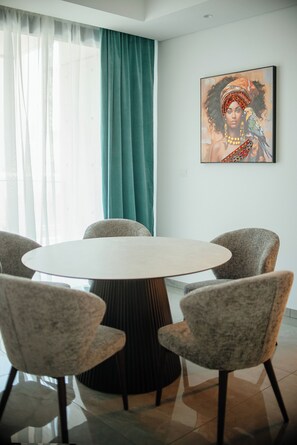 Un coin repas comprenant une table ronde, quatre chaises, un rideau de couleur turquoise et une œuvre d’art encadrée accrochée au mur.