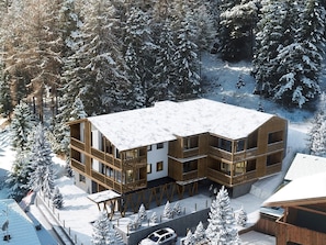 Eine moderne Holzlodge mit mehreren Balkonen, umgeben von schneebedeckten Bäumen.