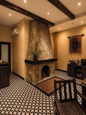 A stone fireplace with a mantel, a tiled floor with a geometric pattern, and a wooden bench.