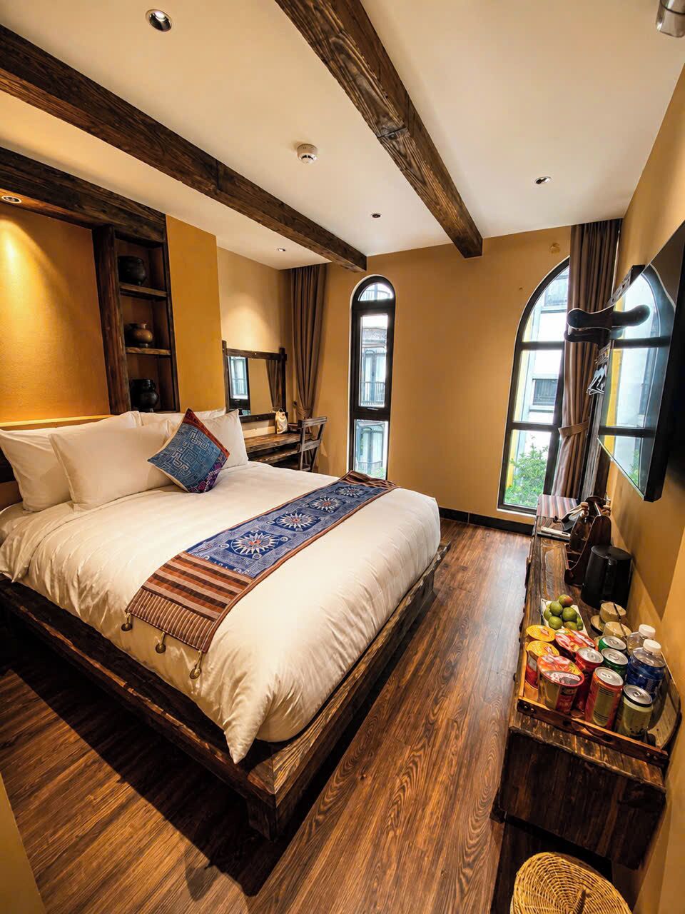 Un dormitorio con una cama grande, vigas de madera, una ventana y una mesita de noche con lámpara.