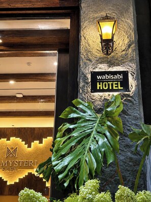 A hotel entrance with a sign reading 'Wabisabi HOTEL' and a large plant in the foreground.
