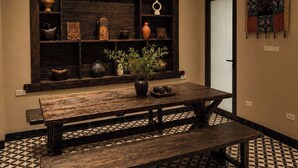 Una habitación con un banco de madera, piso de baldosas y una estantería con diversos objetos.