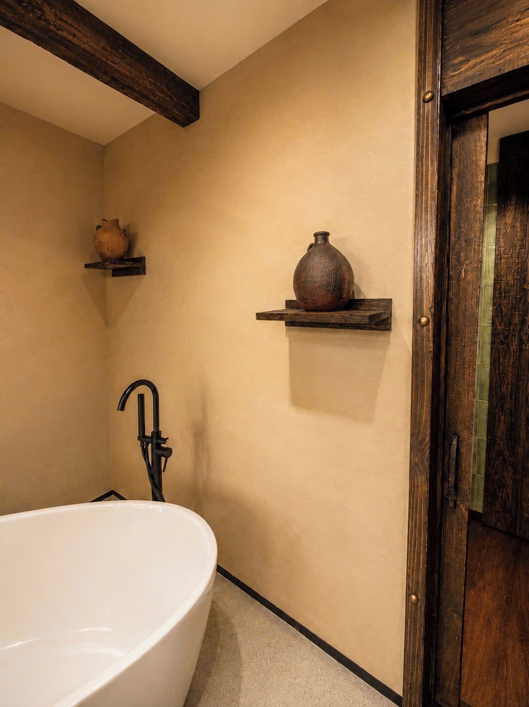 Une salle de bain avec une baignoire sur pieds, des poutres en bois au plafond et deux étagères ornées de vases décoratifs.