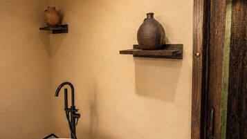 A bathroom with a freestanding bathtub, wooden beams on the ceiling, and two shelves with decorative vases.