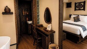 A bedroom with a bed, a bedside table, a mirror, and a wall-mounted quilt.