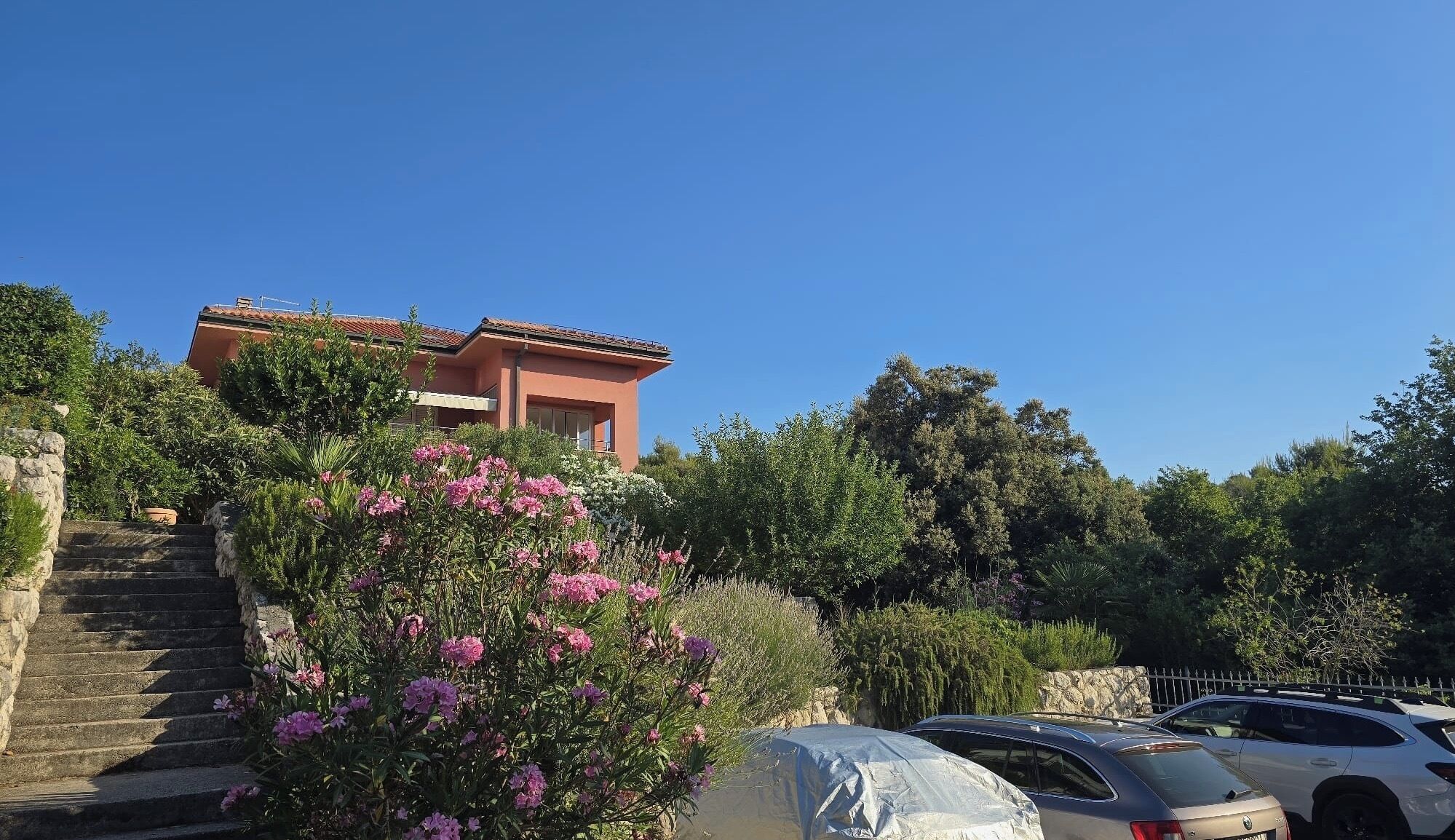 Un bâtiment avec un toit rouge, entouré de verdure et de voitures garées.