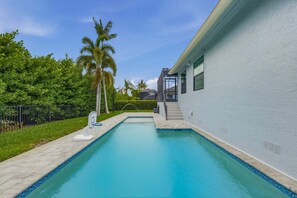 A swimming pool with a clear blue water, surrounded by a white building and palm trees. - 4BR Marco Island home with heated pool, WiFi, and room for 8 (Marco Island)