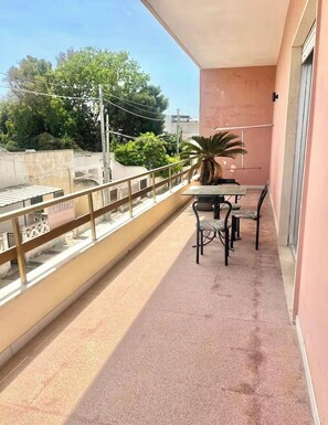 A balcony with a table and chairs, a potted plant, and a view of trees and buildings. - Spacious and bright apartment in the center of Torre dell'Orso with private parking space (Torre dell'Orso)