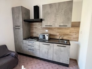 A compact kitchen with grey cabinets, a microwave, a gas stove, and a black range hood. - Spacious and bright apartment in the center of Torre dell'Orso with private parking space (Torre dell'Orso)