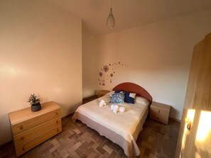 Ein Schlafzimmer mit einem Bett, einer hölzernen Kommode, einem Nachttisch, einer Wanddekoration und einer Pendelleuchte.