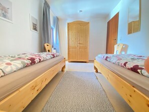 Ein Zimmer mit zwei Holzbetten, einem Schrank, einem Stuhl und einem Spiegel an der Wand.