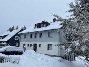 Ein zweistöckiges Wohngebäude mit verschneitem Dach und einer sichtbaren Haustür.