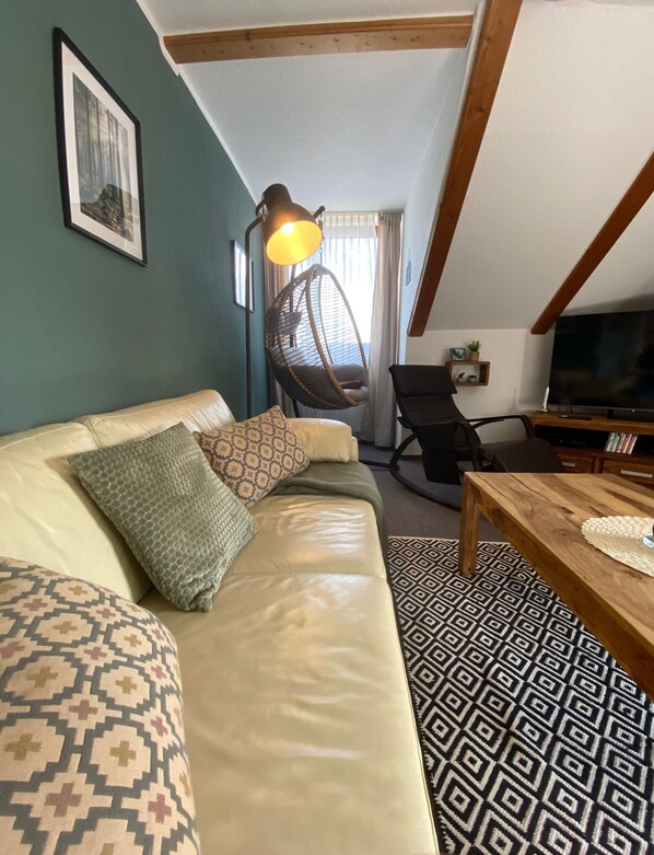 Ein gemütliches Wohnzimmer mit einer Couch, einem Hängesessel, einem Holztisch und einem Fernseher.