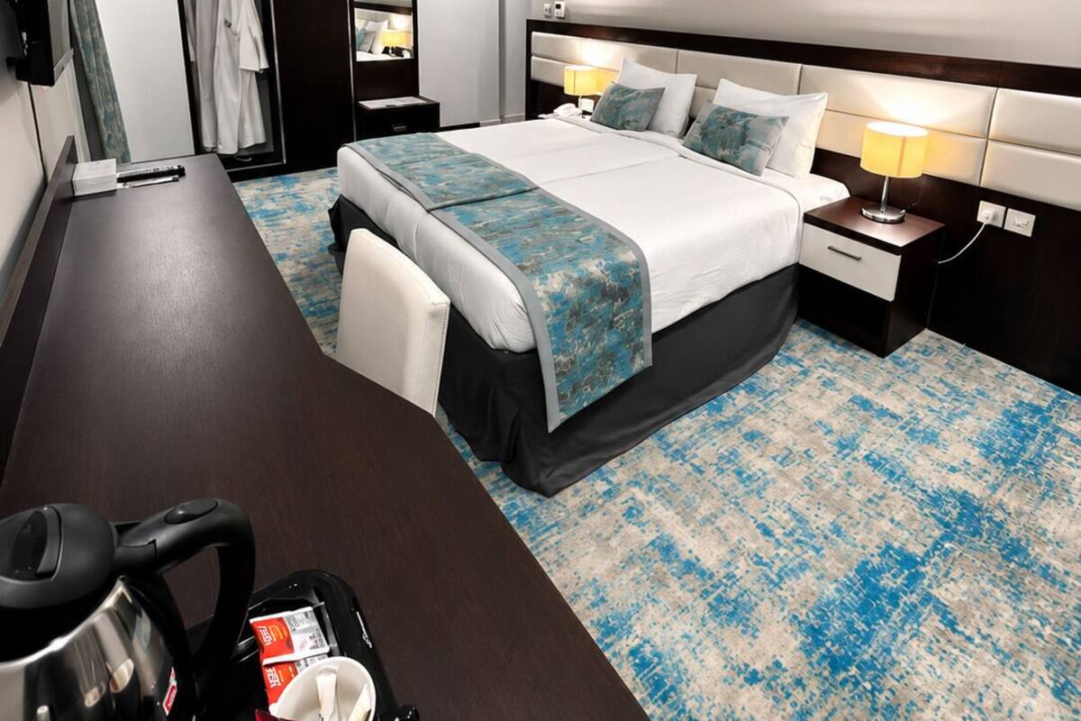 Une chambre d’hôtel comprenant un lit, des tables de chevet, un bureau, une chaise, une armoire et un tableau au mur.