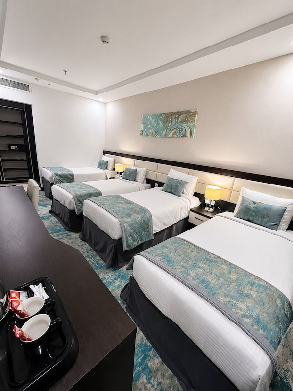 A hotel room with three beds, a desk with a tray of items, and a painting on the wall.
