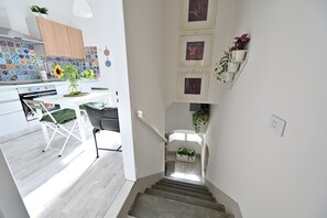Uma cozinha moderna com revestimento de azulejo, um espaço de refeições com mesa e cadeiras, e uma escada com prateleira para plantas.
