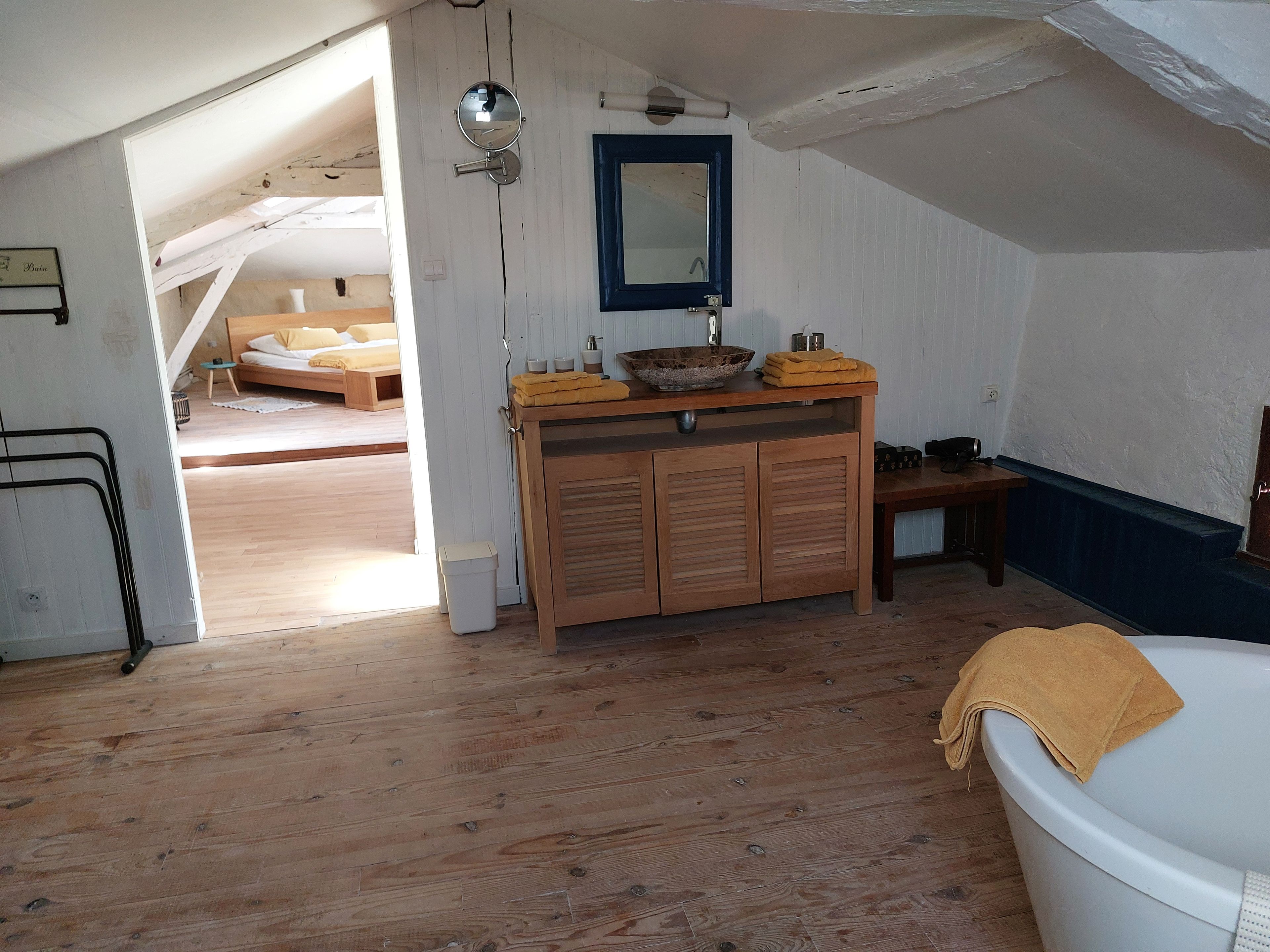 Een kamer met een houten vloer, een witte badkuip, een houten bankje en een klein tafeltje met een kom en handdoeken.