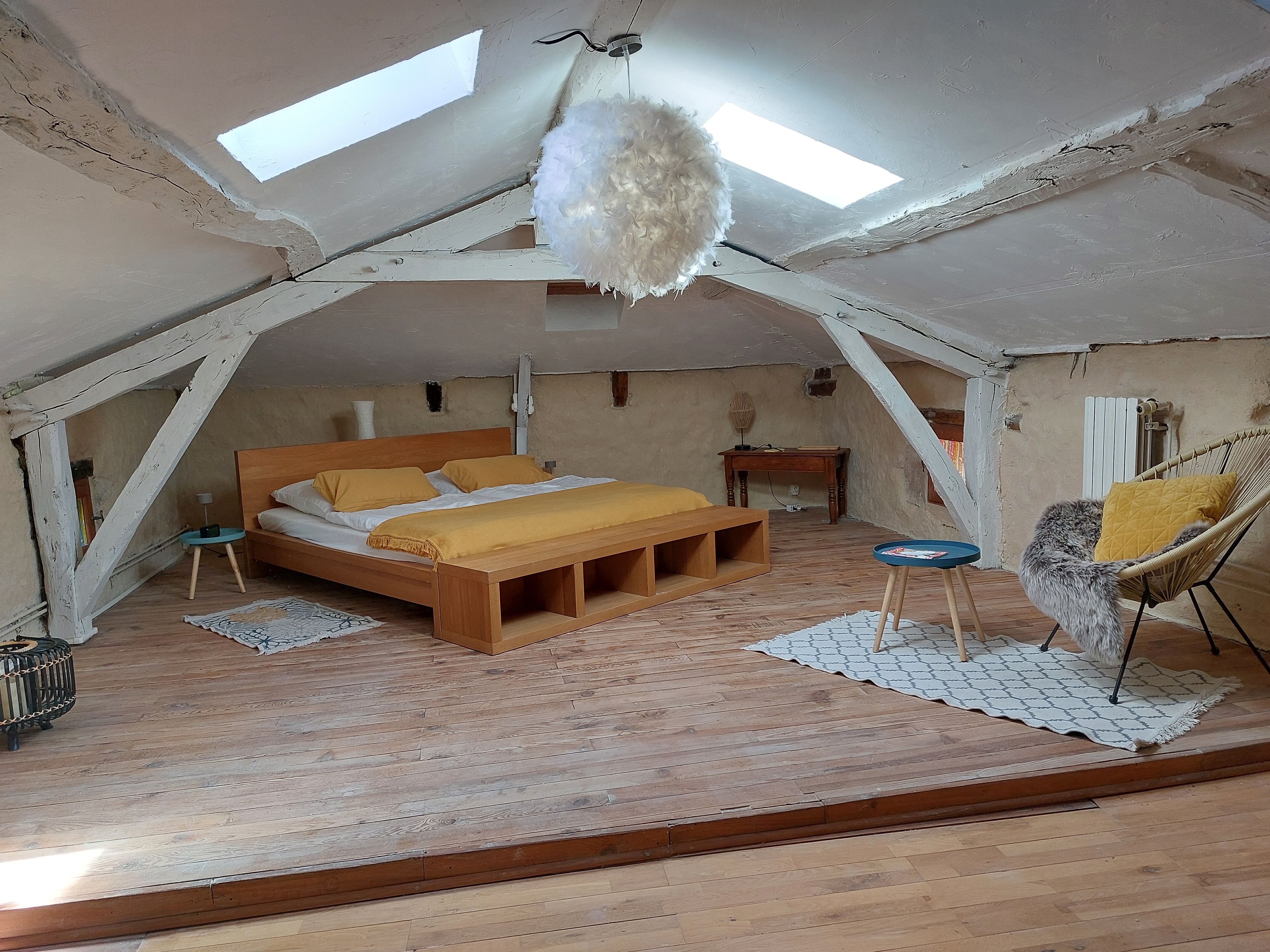 A bedroom with a wooden bed, a hanging light fixture, a chair, and a small table.
