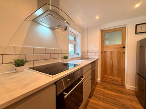 A modern kitchen with a built-in stove, a wooden door, and a window. - Unique Devon Cottages - Sunset Cottage (Exmouth)